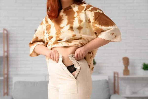 Image of woman trying to do her trousers up after pregnancy weight gain England